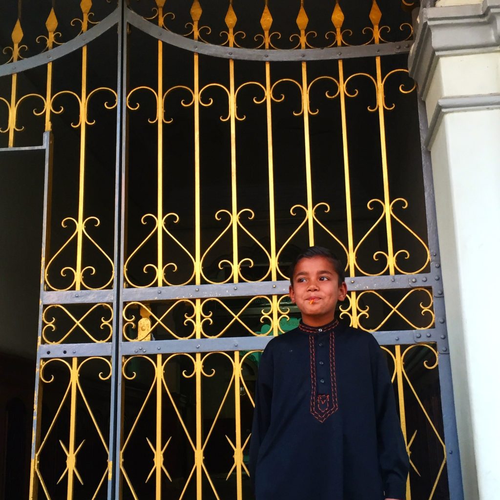 Young boy in black robe standing in front of gold gate of a mosque