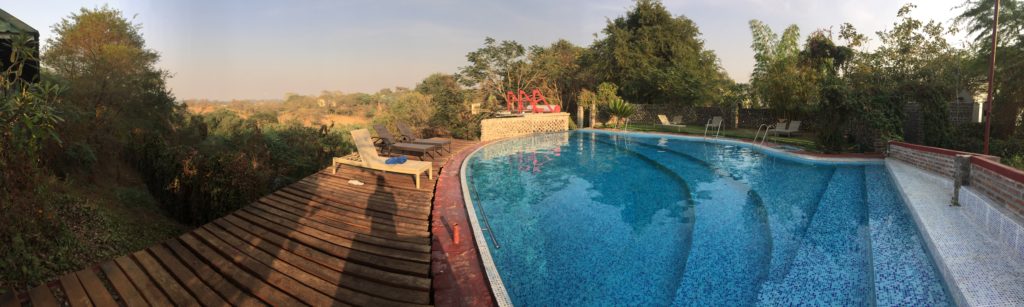 Panoramic photo of the in-ground pool surrounded by green trees and a view of Yenangyaung in the background