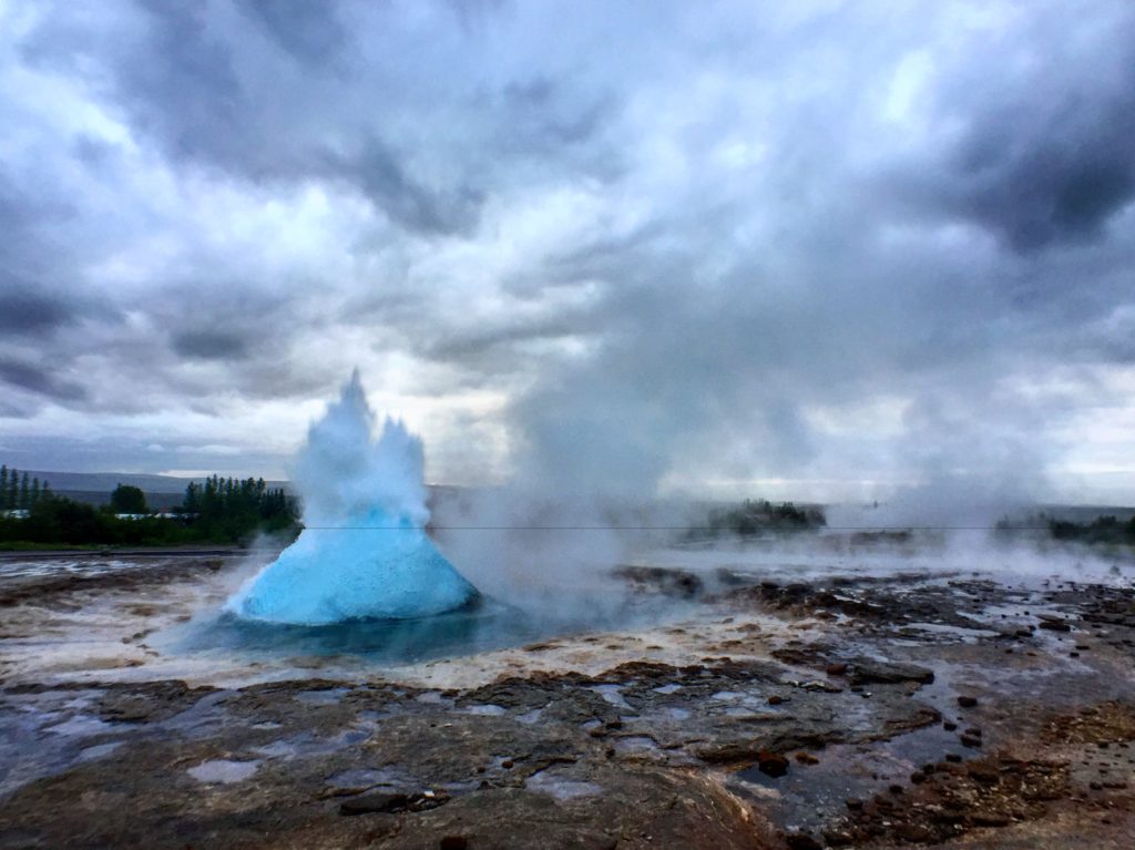 A neon blue geyser in the process of exploding into the cloudy early morning sky