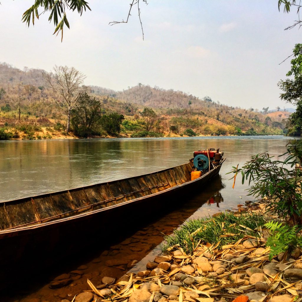 A long boat tied up at the edge of a wild river