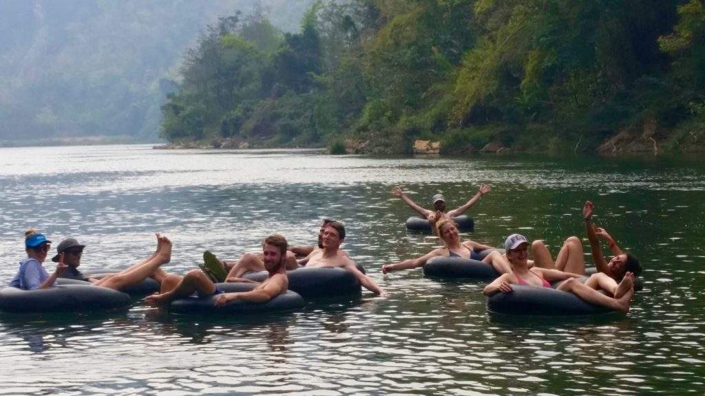 Ten tourists in inner tubes wave from the middle of a river