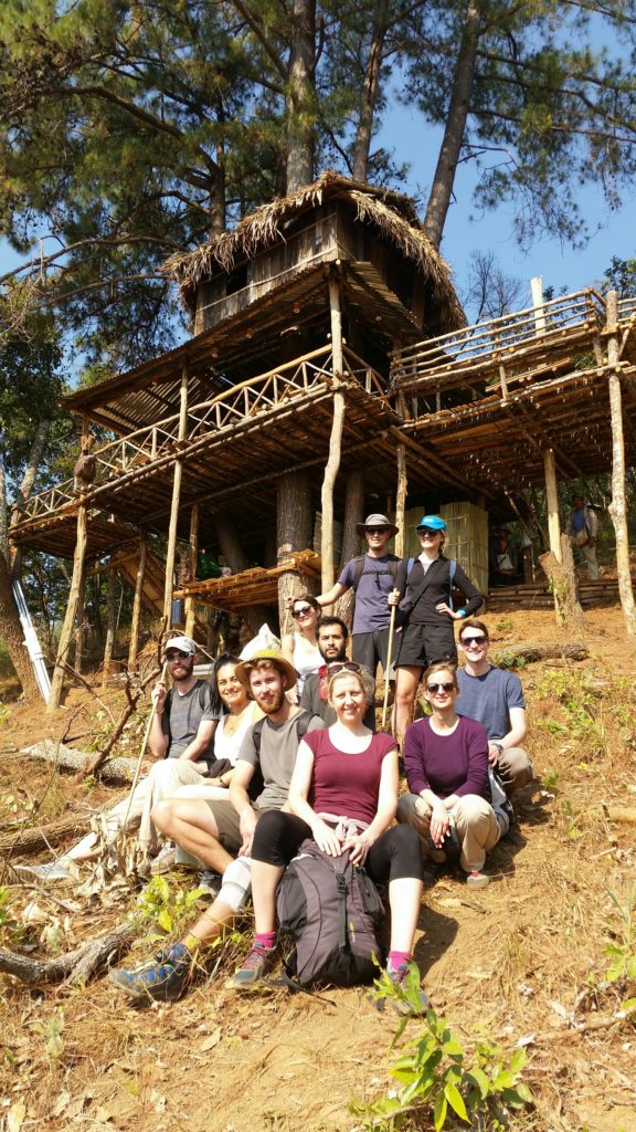 Ten tourists pose for a group photo in front of a bamboo treehouse