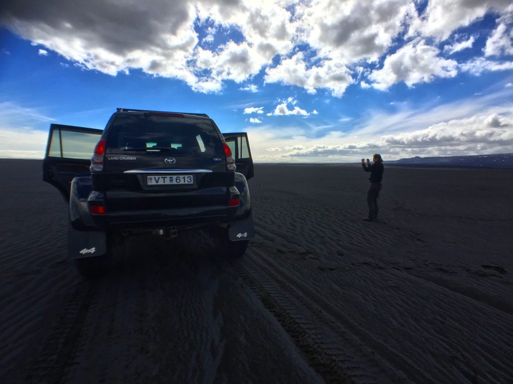A specially modified SUV with large wheels is parked atop black sand