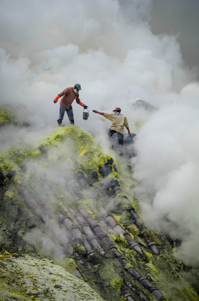 Miners carrying mined sulphur amidst the fumes at Kawah Ijen