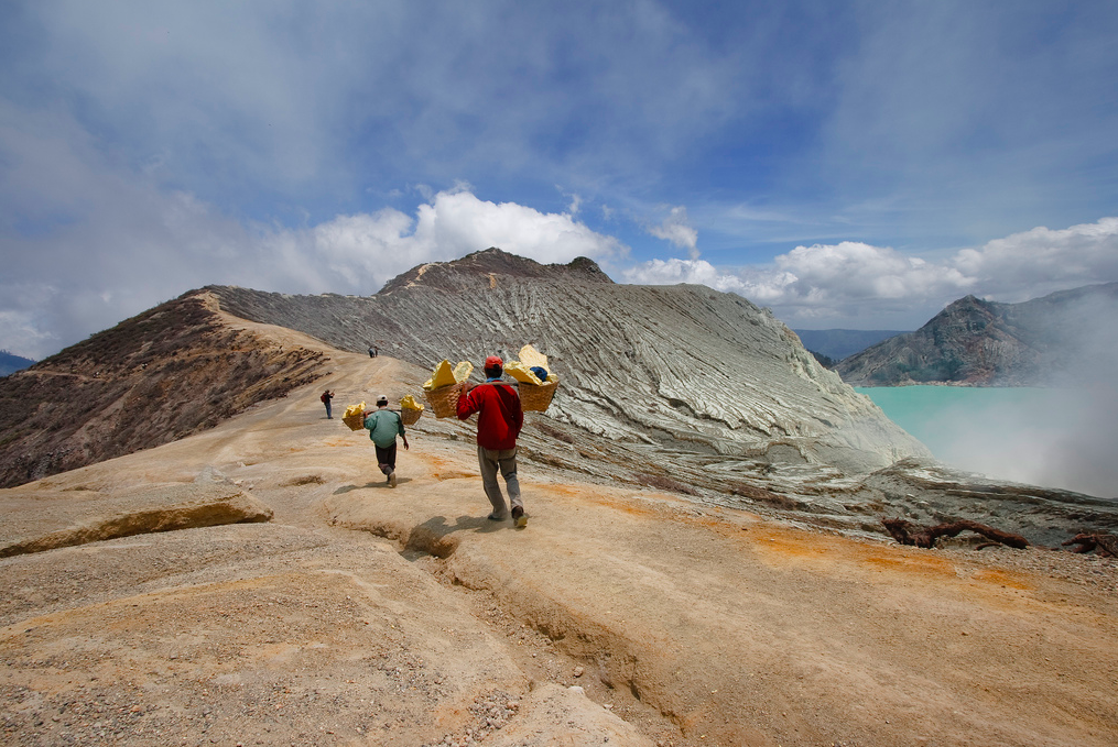 Miners walk with loads of sulphur in wicker baskets along the slops of a volcano