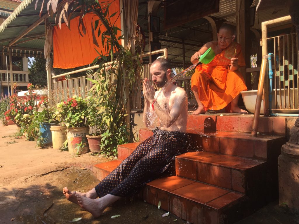 Me sitting on the steps of Wat Po Bantey Chey while an orange robed monk pours water over my head