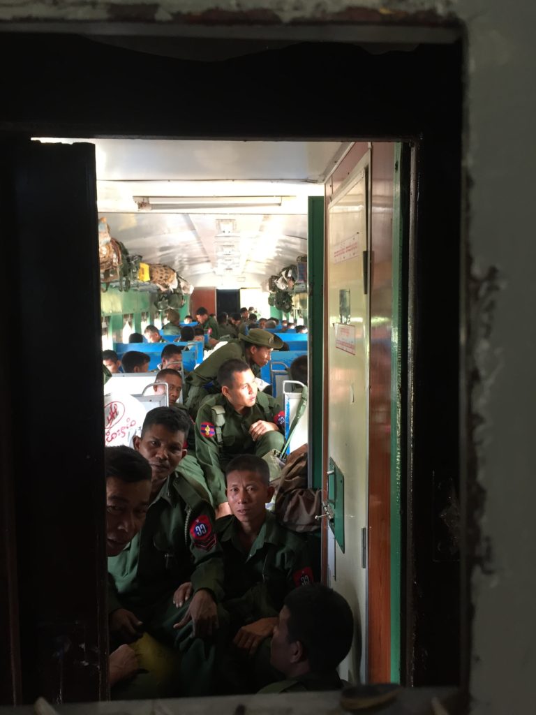 Looking through the window at Burmese military that fill the adjacent train carriage