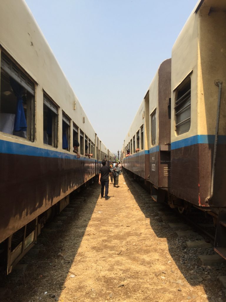 Two trains sit parallel to each other at a stop along the route between Hsipaw and Pyin Oo Lwin