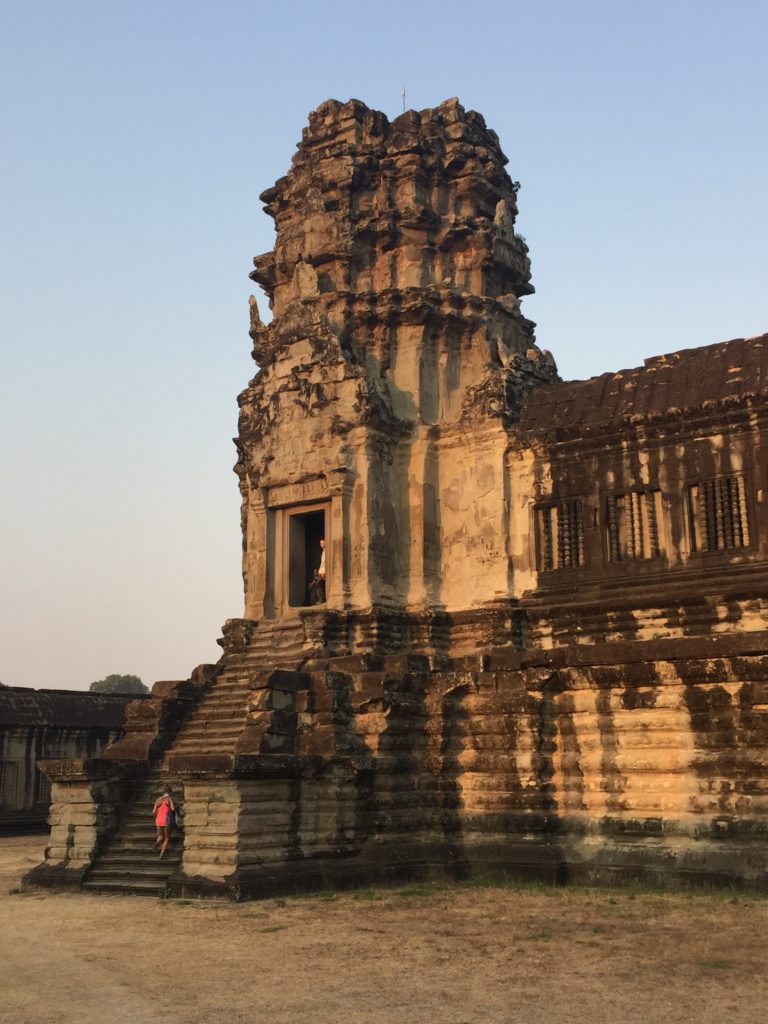 Corner tower of Angkor Wat temple with a lone traveler walking up the steps