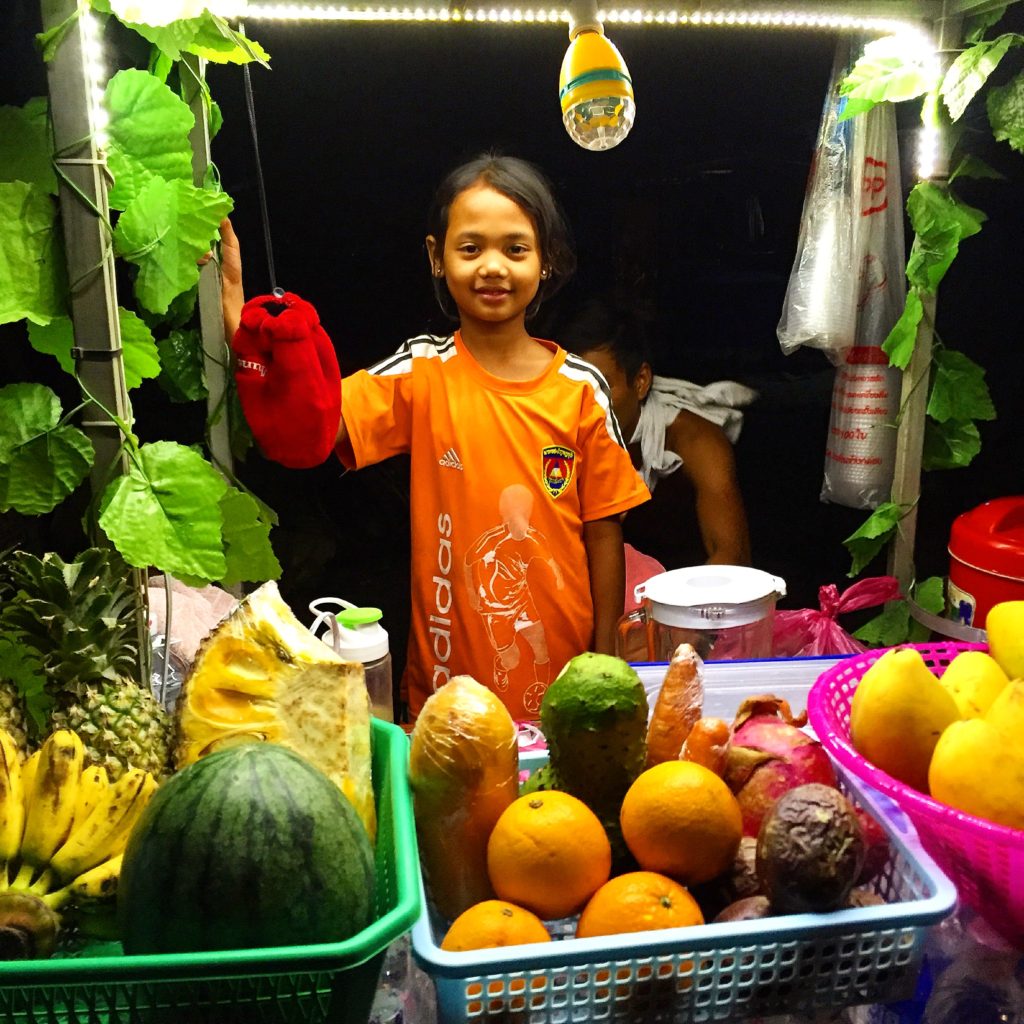 Young girl stands behind fruit & smoothie cart, Siem Reap, Cambodia