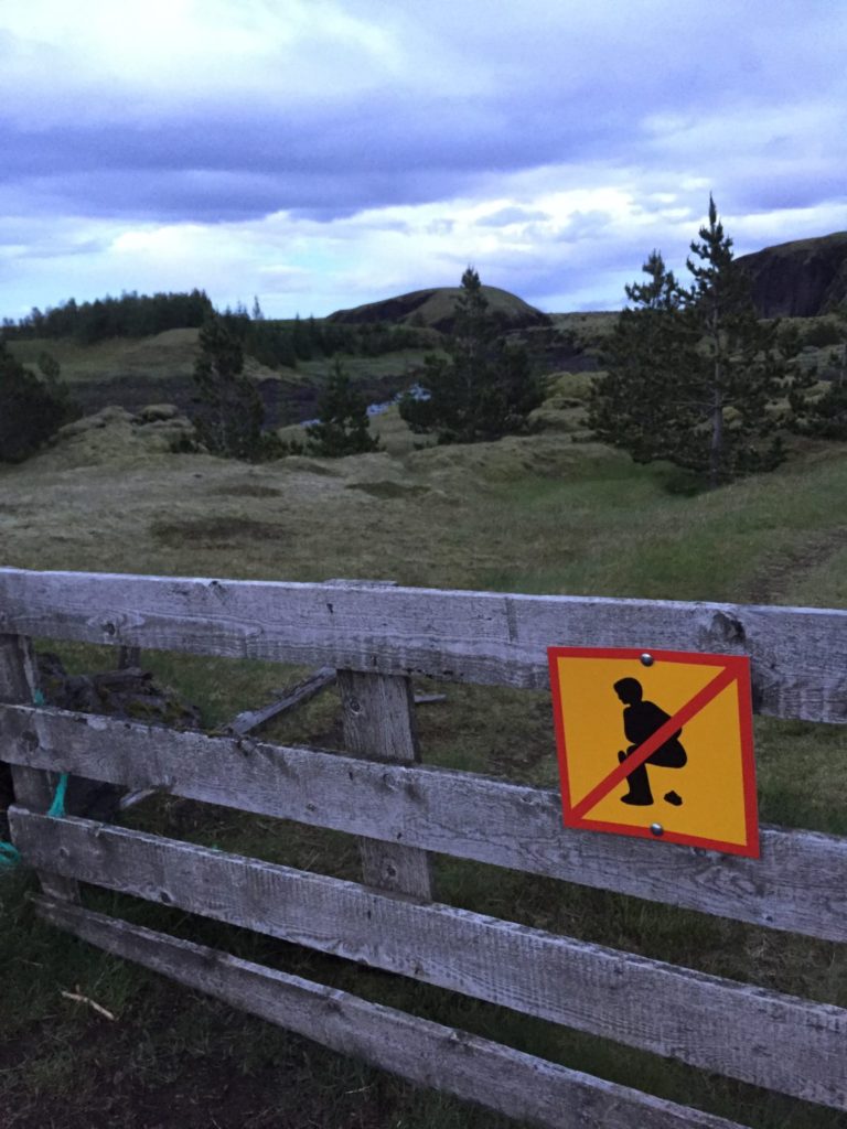 No pooping sign tacked on a fence with rolling hills and purple sky in the background