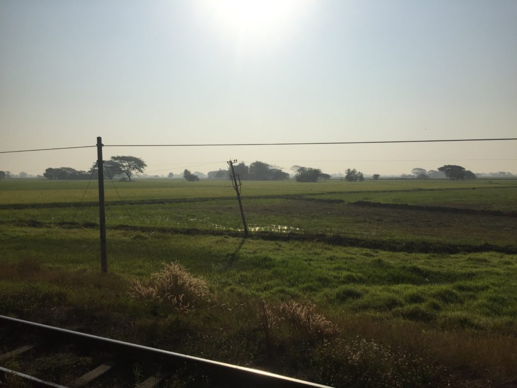 Railway track, green fields and blue sky view from the train