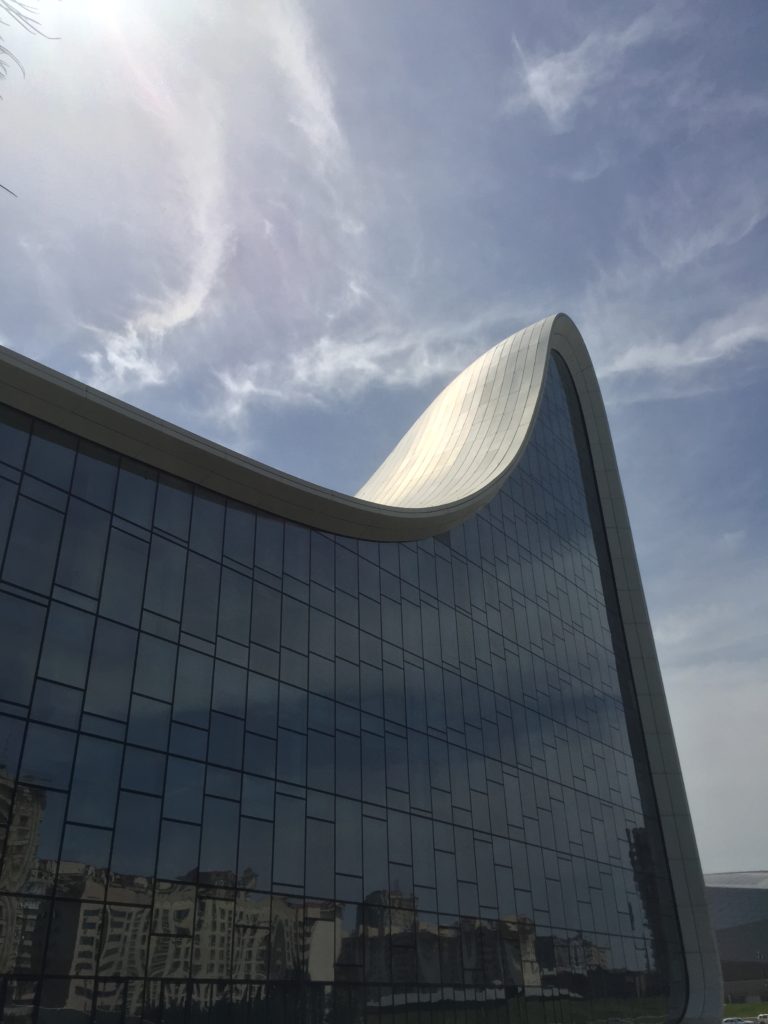 Large wall of reflective glass with curving white roof and blue sky above