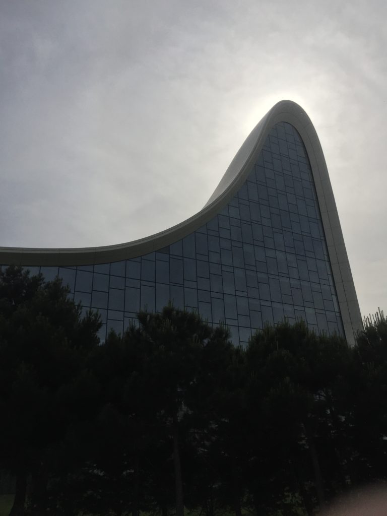 Up view of the large wall of glass of the Heydar Aliyev Center with sun hiding behind the top